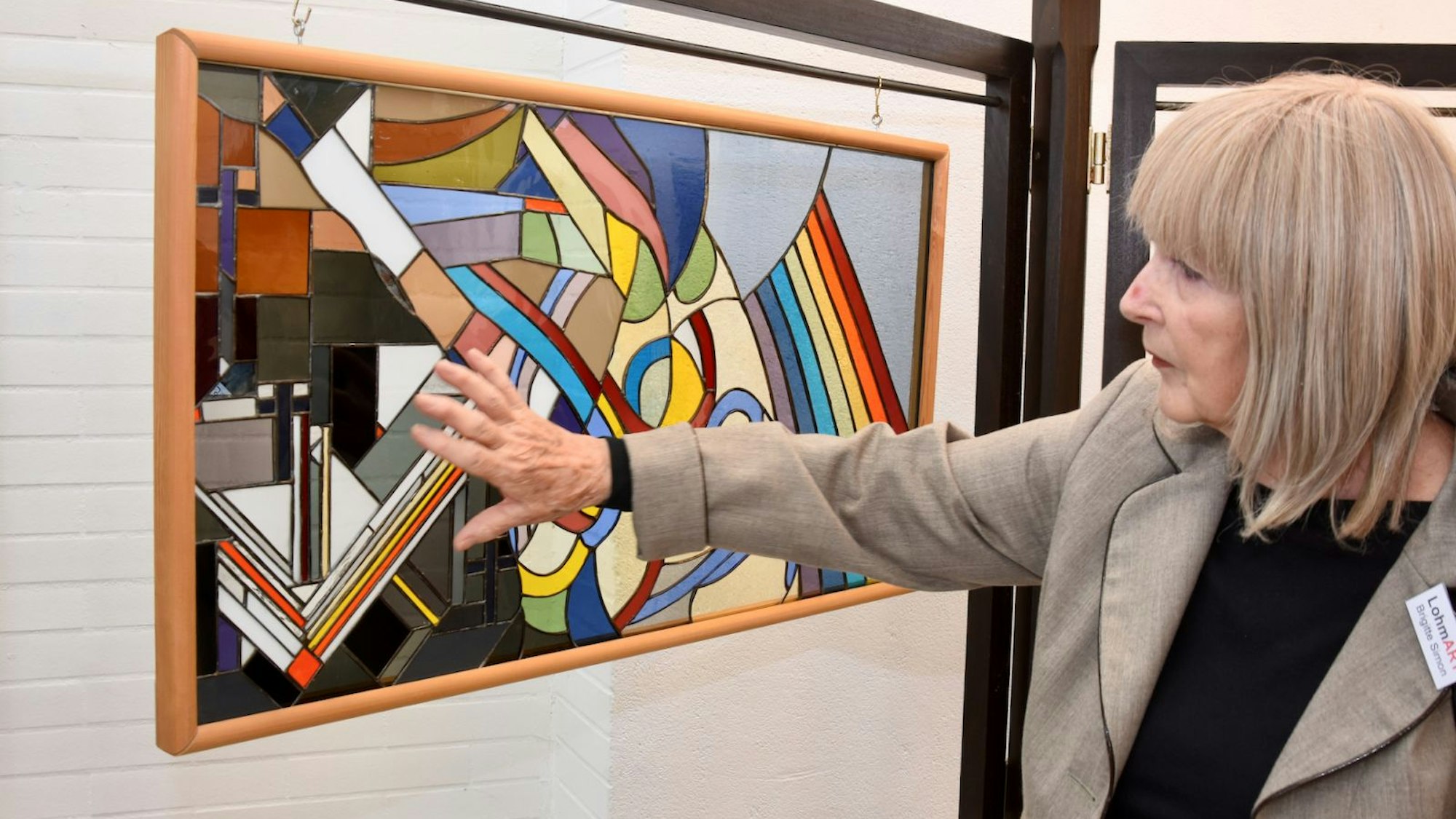 Eine blonde Frau hält ihre Hand über ein Glasbild aus leuchtenden Farben.