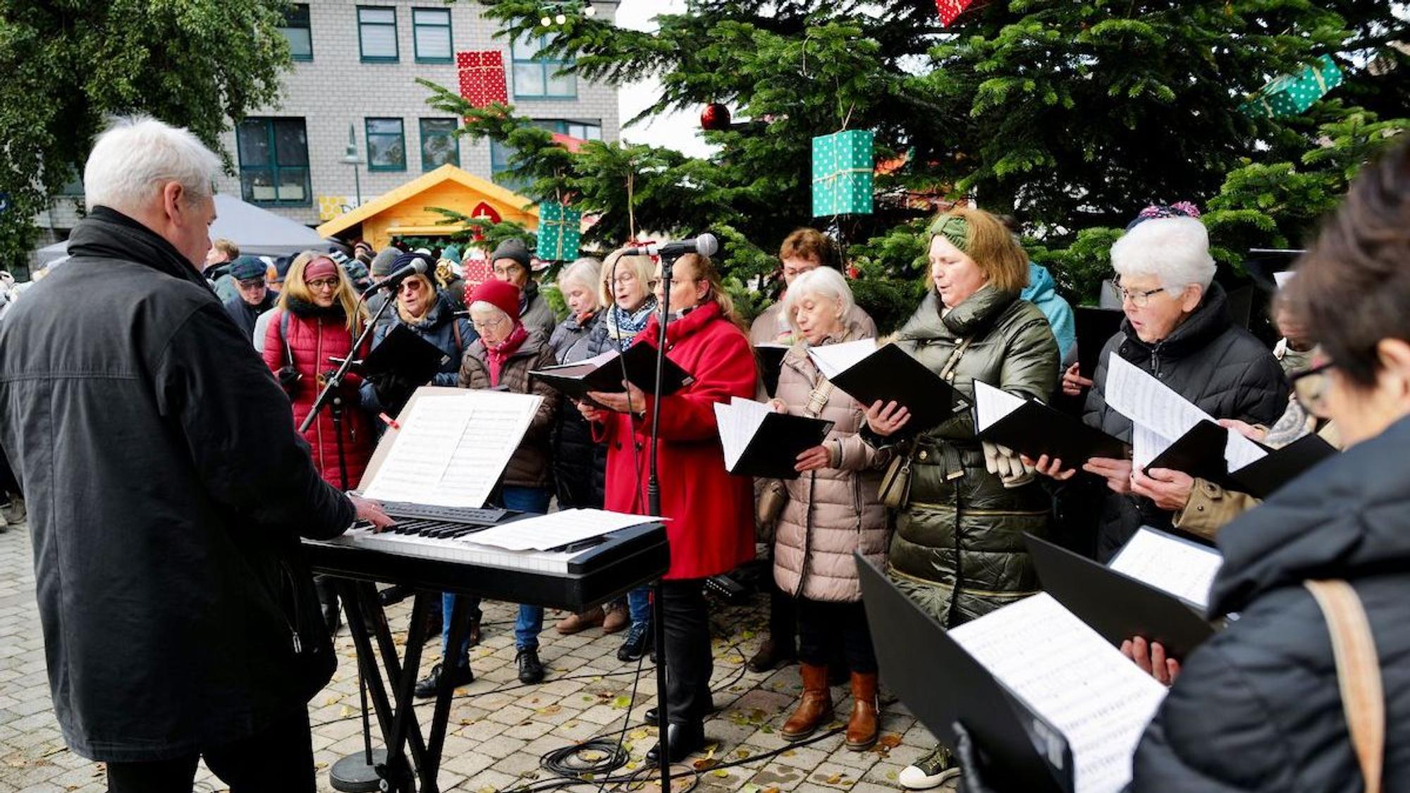 Ein Chor singt am ersten Adventswochenende 2023 vor einem großen Weihnachtsbaum beim Adventsmarkt auf dem Mondorfer Adenauerplatz.