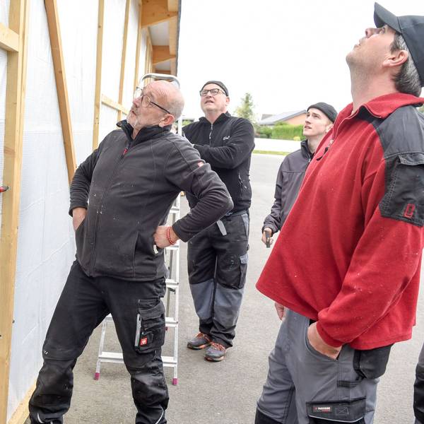 Männer stehen vor einer provisorischen Wand aus einem Holzgerüst und einer Plane.