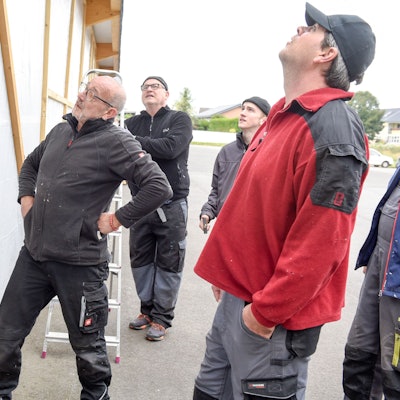 Männer stehen vor einer provisorischen Wand aus einem Holzgerüst und einer Plane.