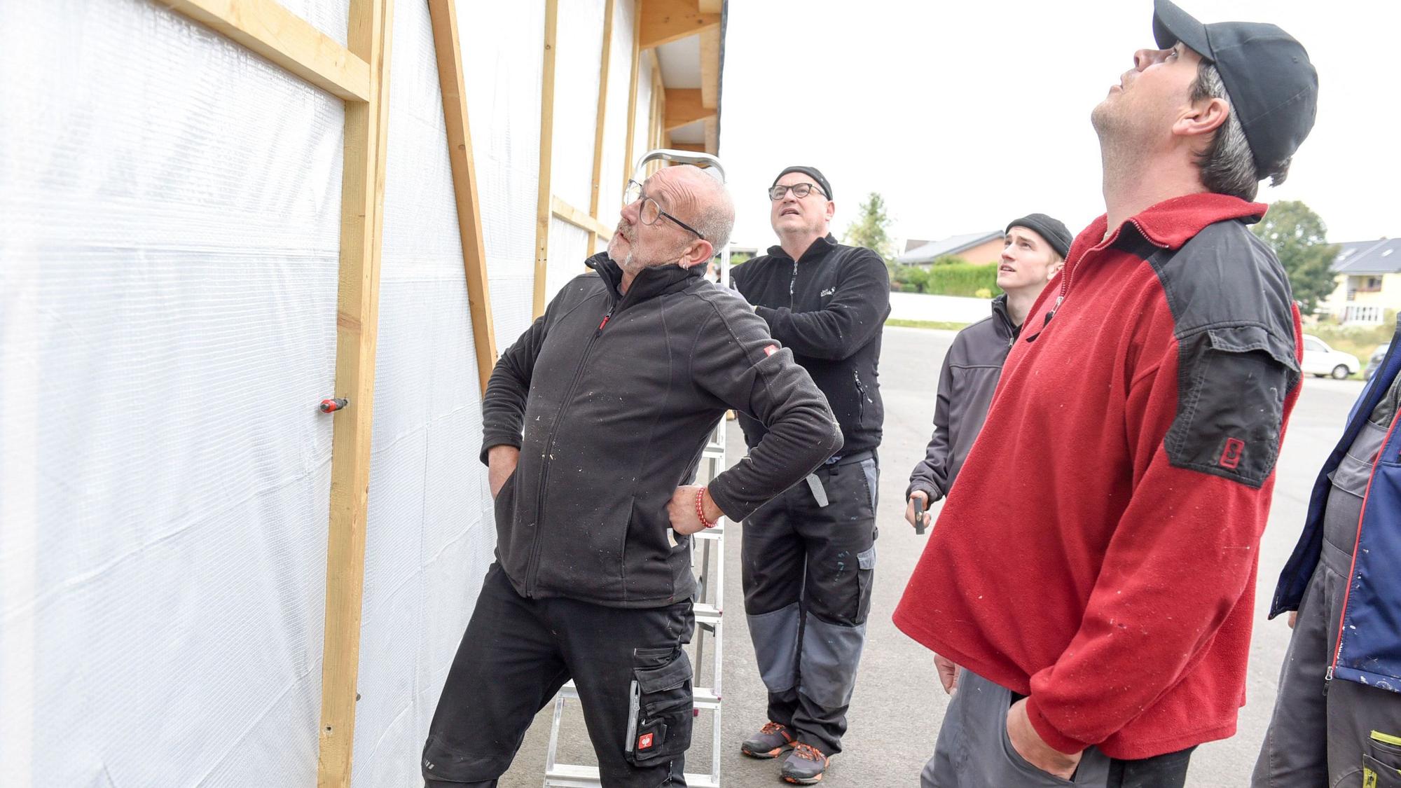 Männer stehen vor einer provisorischen Wand aus einem Holzgerüst und einer Plane.