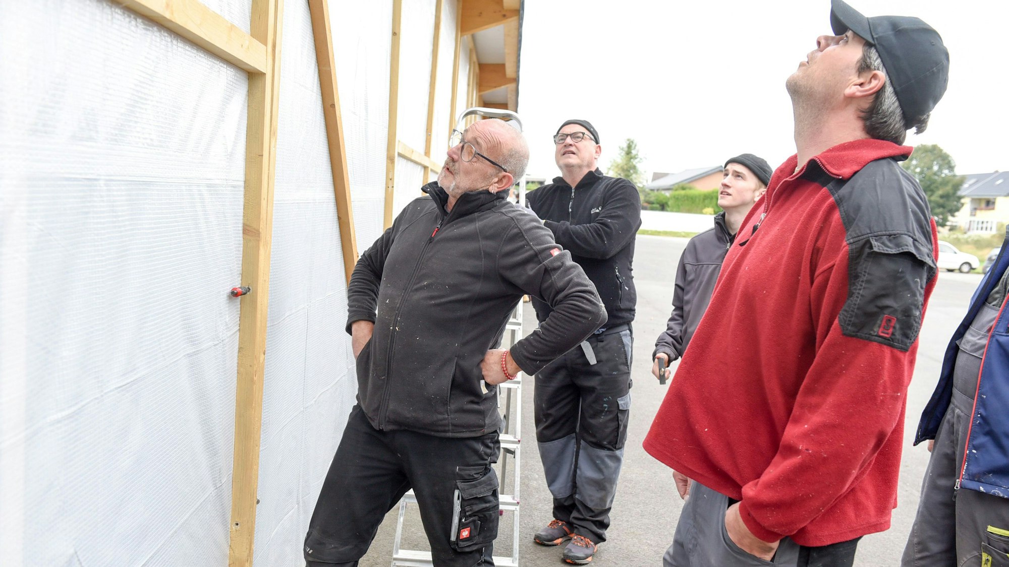 Männer stehen vor einer provisorischen Wand aus einem Holzgerüst und einer Plane.