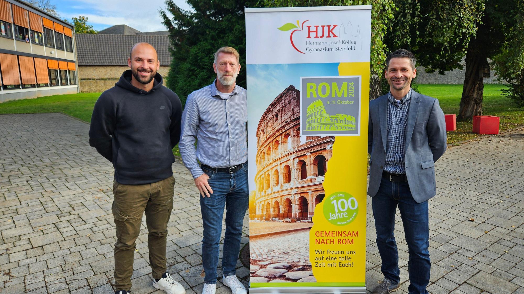 Andreas Winkler, Ralf Kremp und Thomas Frauenkron stehen neben einem Aufsteller, der für die Romfahrt wirbt.