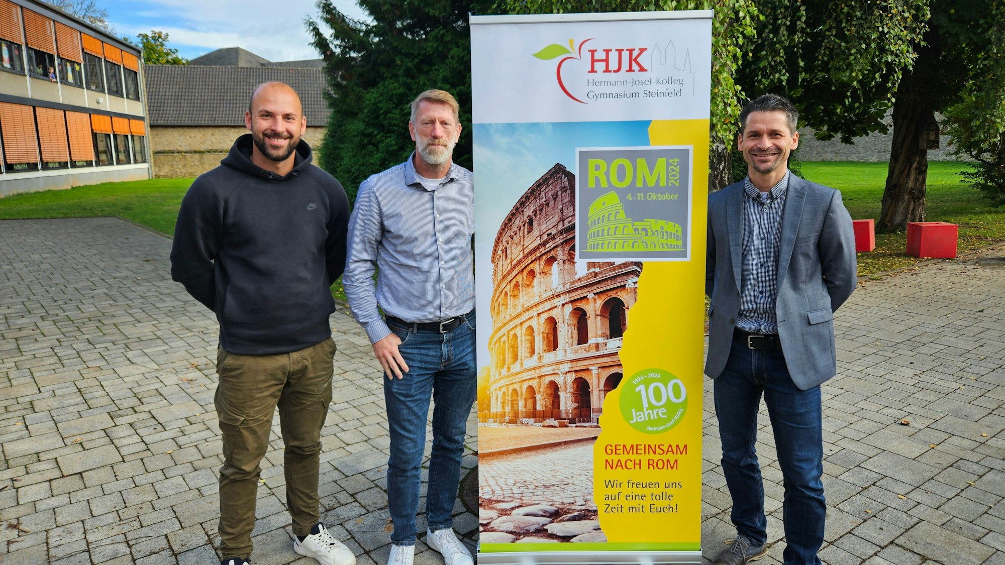 Andreas Winkler, Ralf Kremp und Thomas Frauenkron stehen neben einem Aufsteller, der für die Romfahrt wirbt.