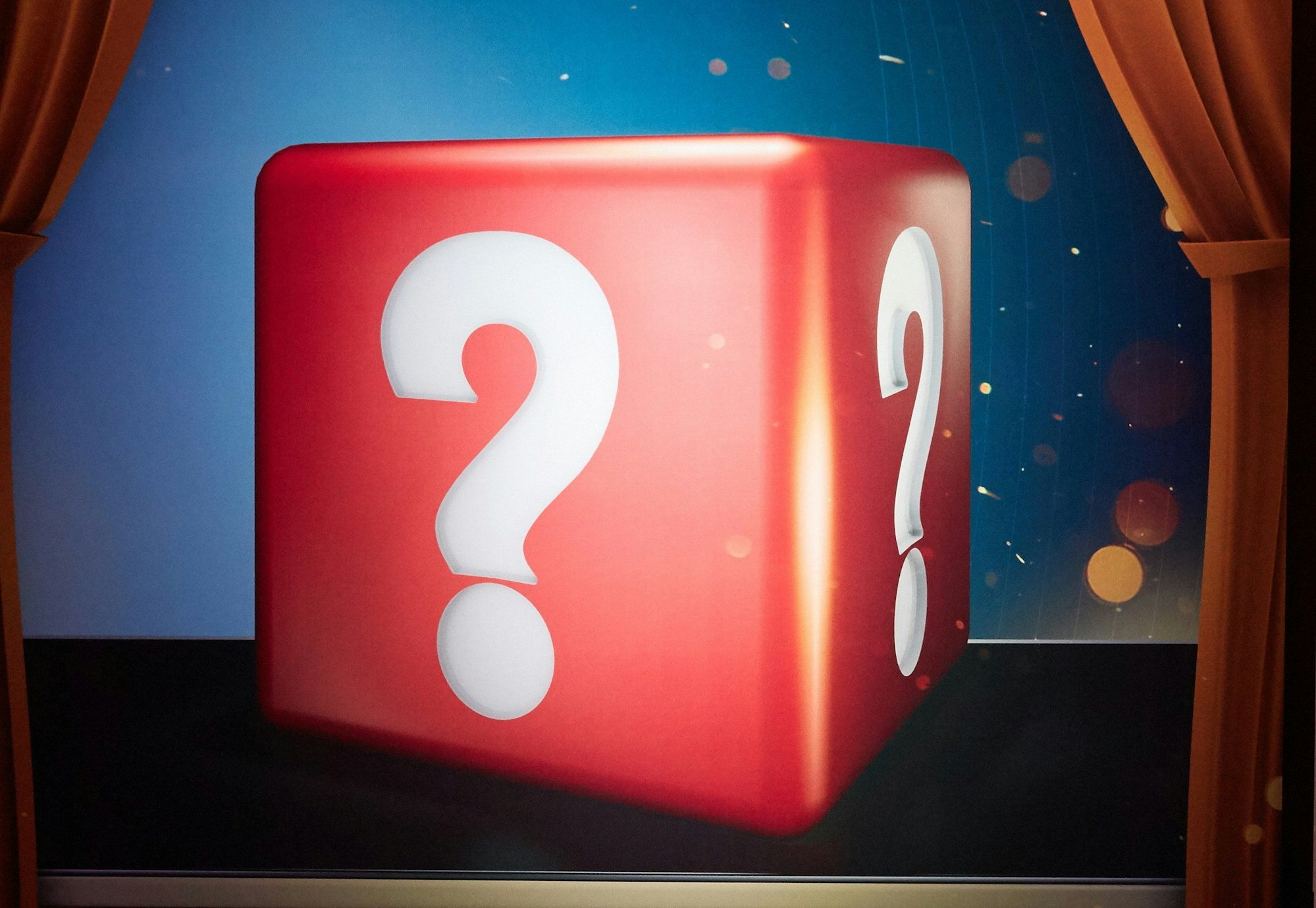 Auf dem Foto ist ein roter Würfel mit weißen Fragezeichen zu sehen.