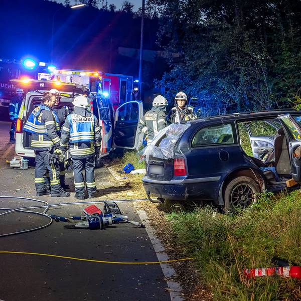 Feuerwehrleute stehen mit Rettungsgerät vor einem Unfallauto.