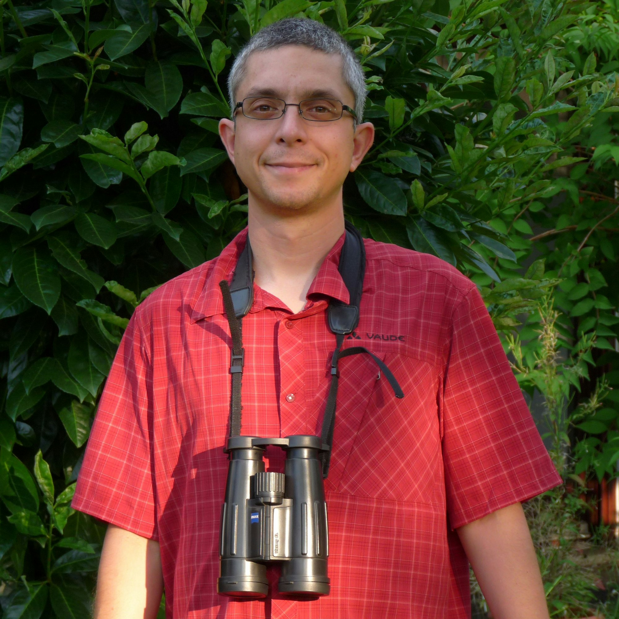 Experte Darius Stiels ist im Porträt in der Natur zu sehen, mit großem Fernglas um den Hals