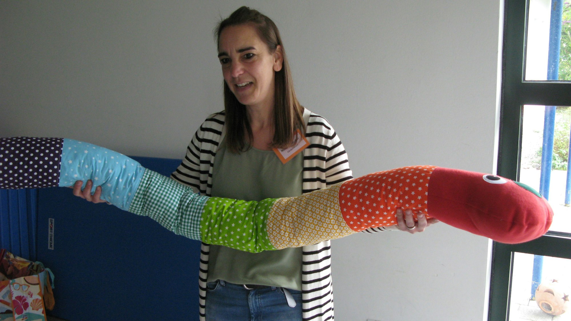 Eine Frau mit einem etwa zwei Meter langen Regenwurm-Stofftier in bunten Farben.