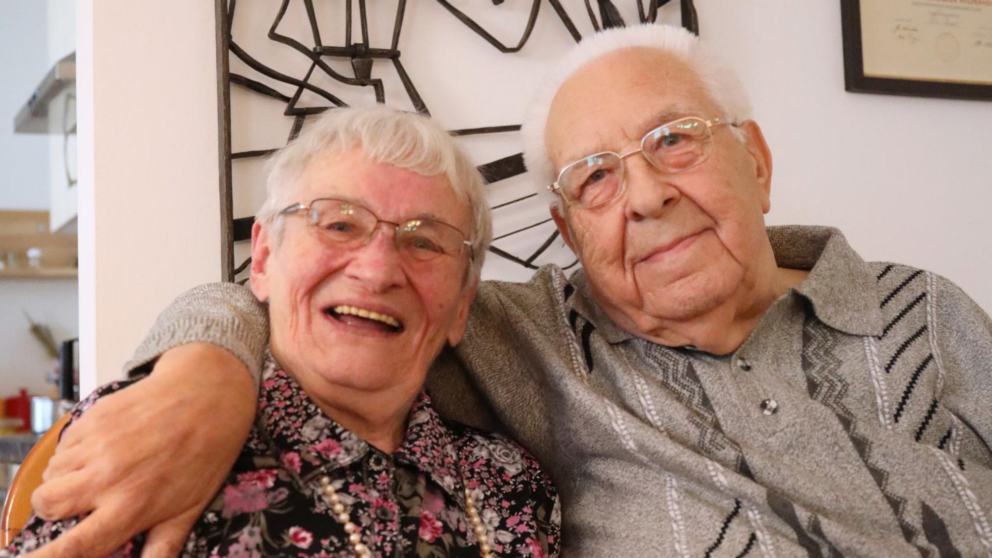 Ein Ehepaar sitzt eng beieinander, der Mann hat seinen Arm um seine Frau gelegt.