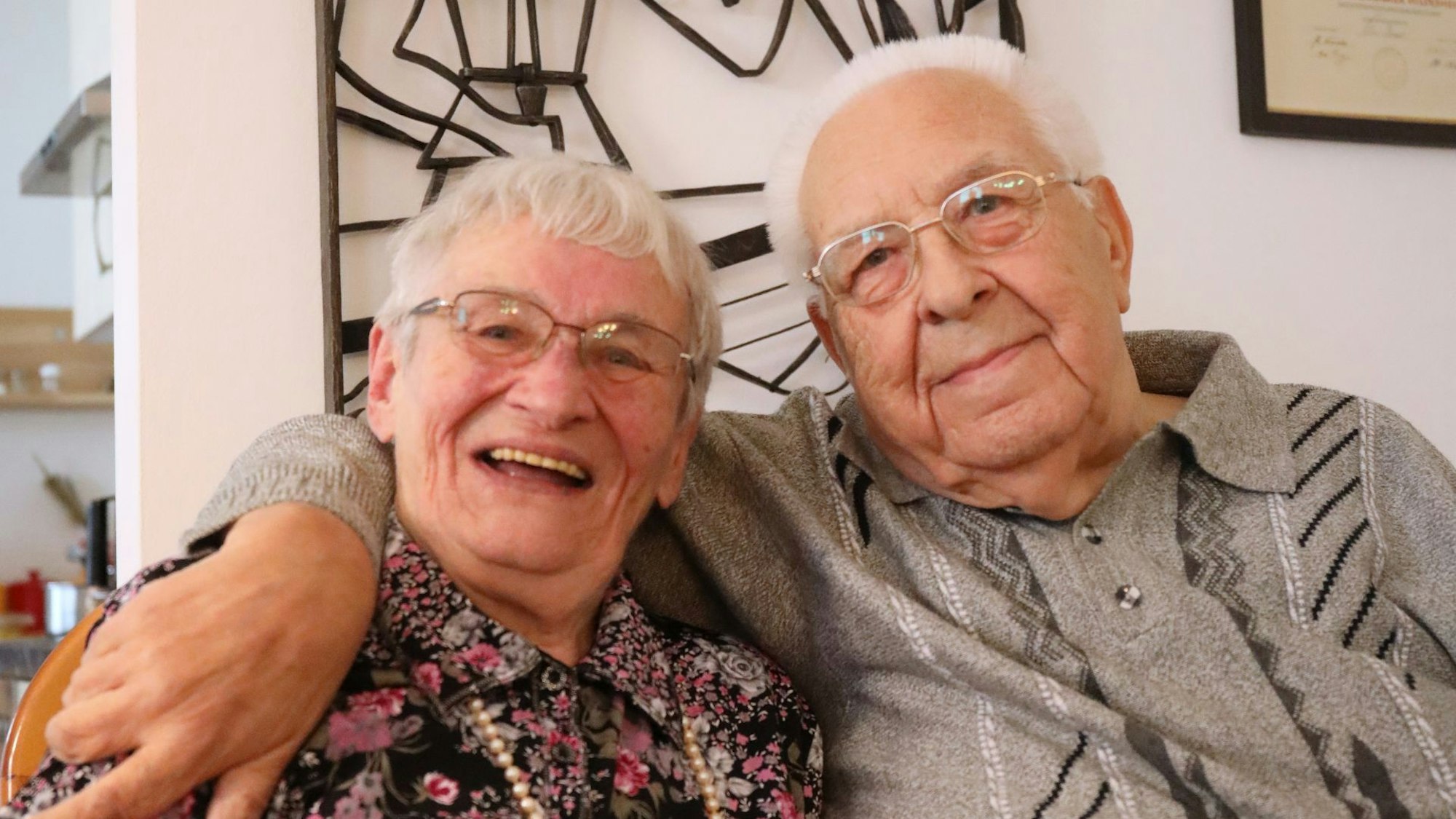 Ein Ehepaar sitzt eng beieinander, der Mann hat seinen Arm um seine Frau gelegt.