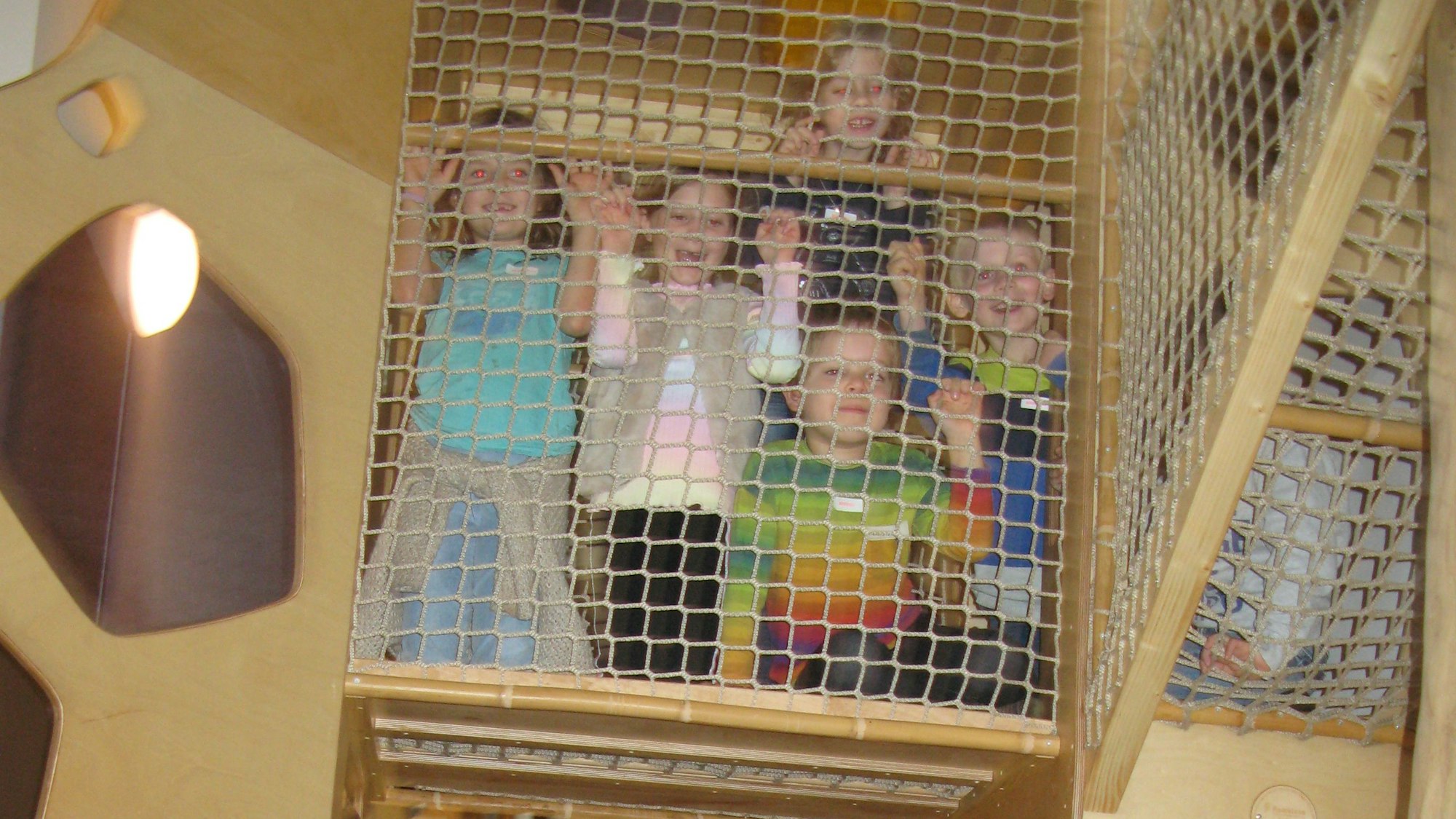 Kindergartenkinder lachen und winken hinter einem Seilnetz.