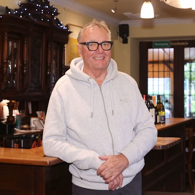 Heiner Welchering steht lächelnd an der Theke in seiner Weinstube.
