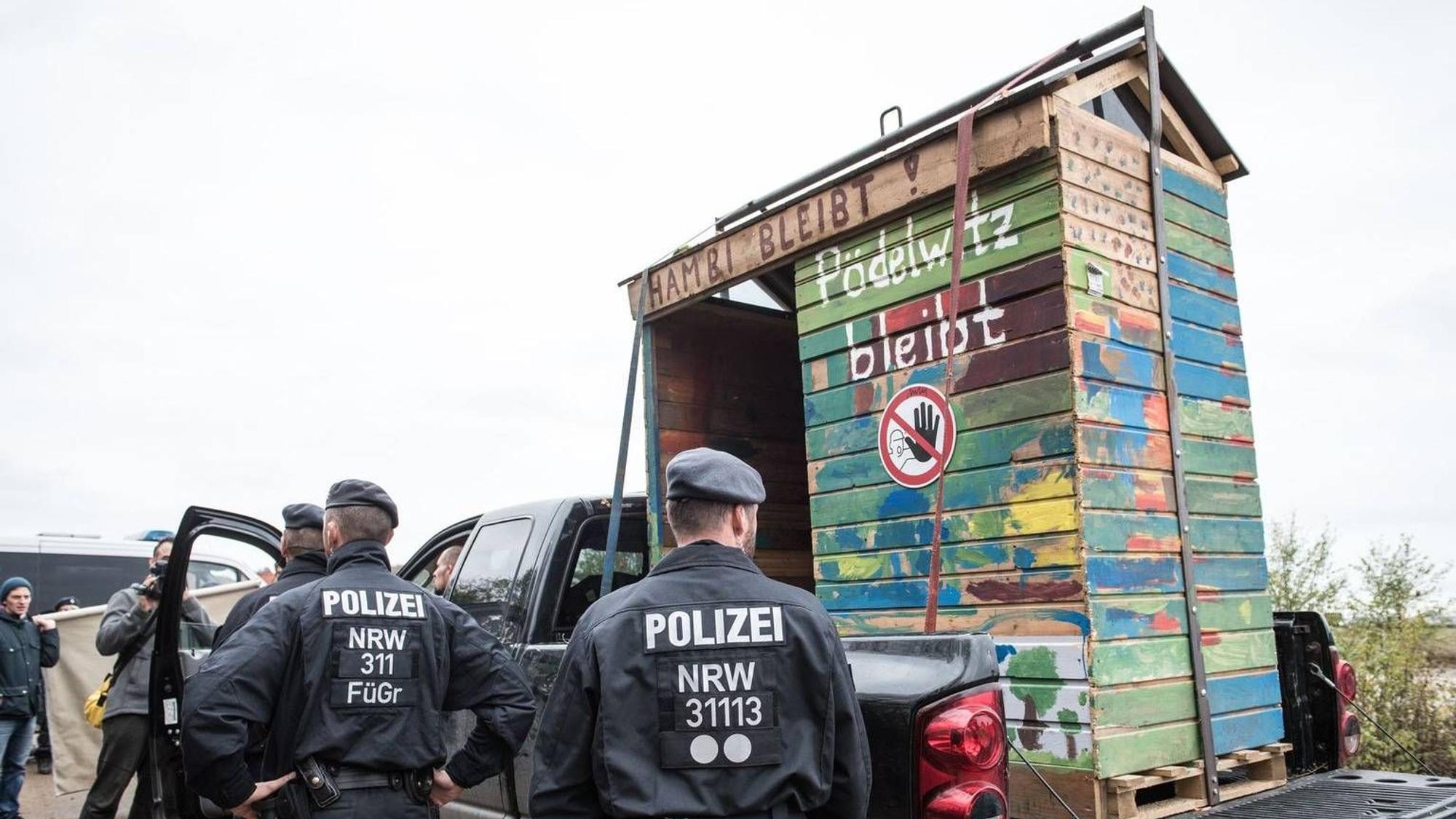 Auf dem Foto ist ein Baumhaus zu sehen, das auf einem Wagen abtransportiert wird. Dabei stehen Polizisten.