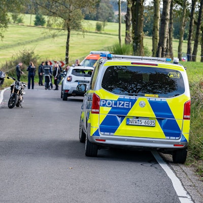 Ein Polizeiauto steht an einem Unfallort. Am Rand der Straße stehen mehrere Motorräder.