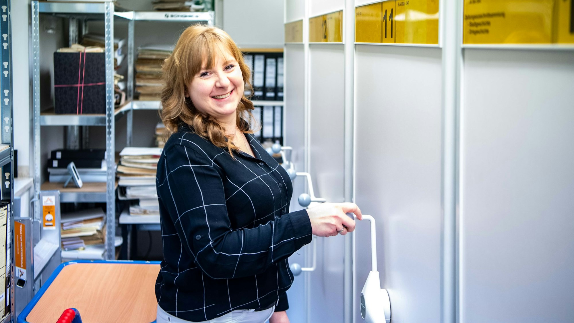 Eine Frau steht an der Kurbel eines Archivschrankes.