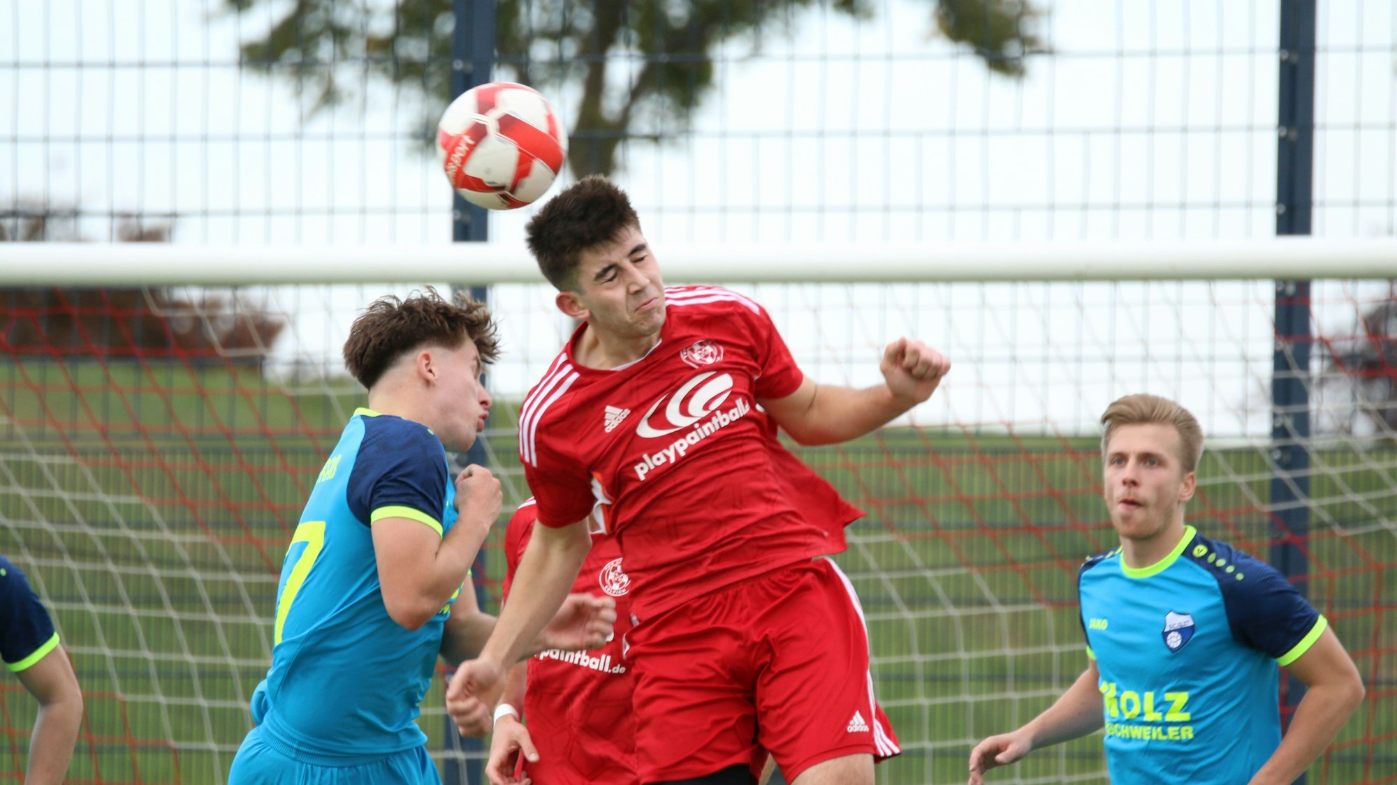 Zwei Spieler steigen zum Kopfballduell hoch, ein anderer beobachtet die Szene.