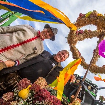 Zwei Männer stehen unter einem geschmückten Erntekranz.
