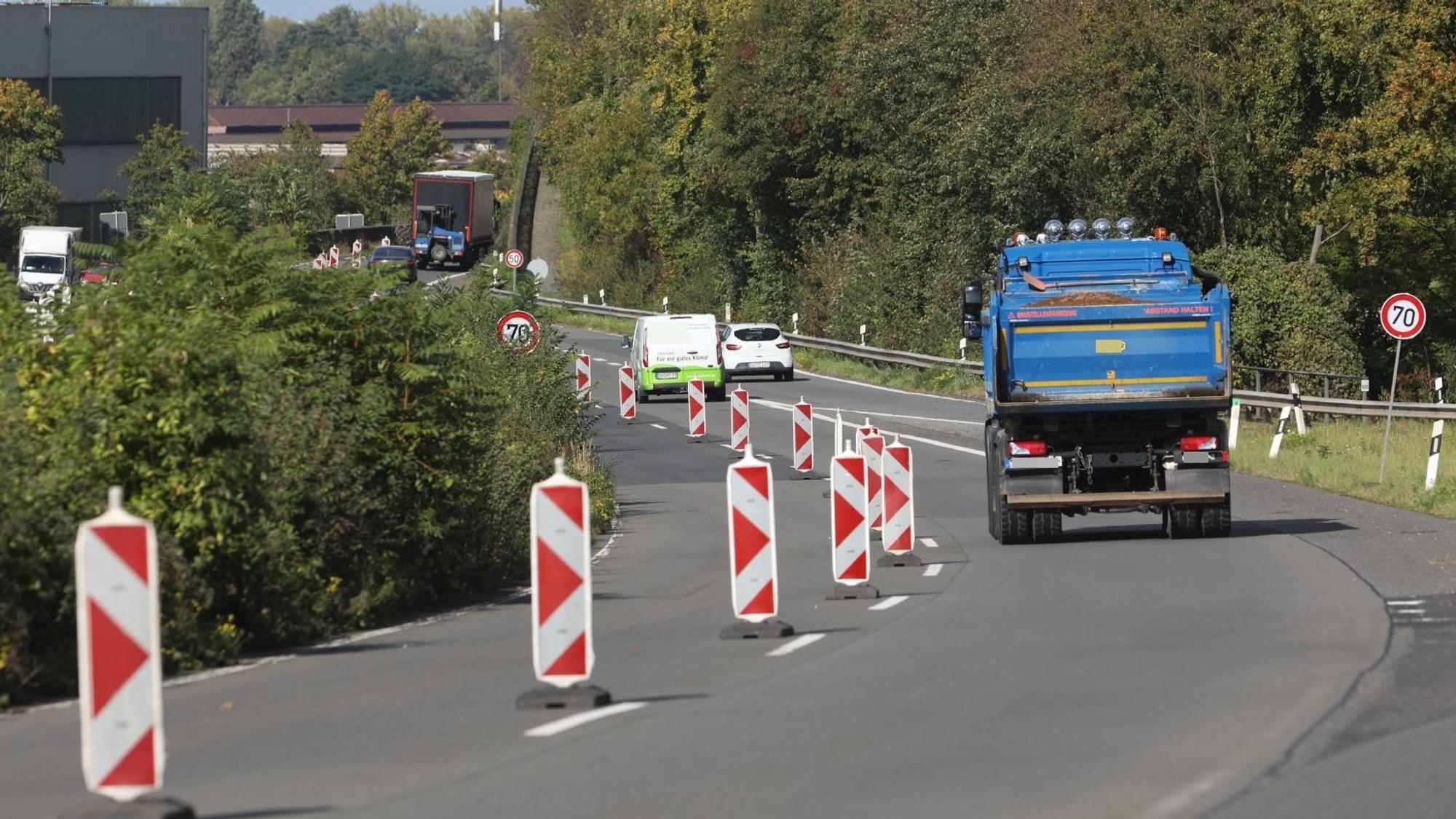 Ein blauer Laster befährt eine zweispurige Straße, die linke Fahrbahn ist durch rot-weiße Baken gesperrt.