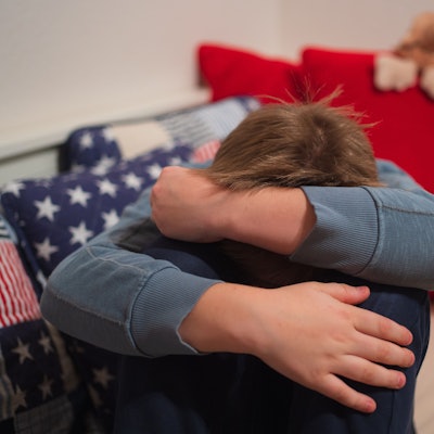 Ein Junge kauert sich auf seinem Bett zusammen.