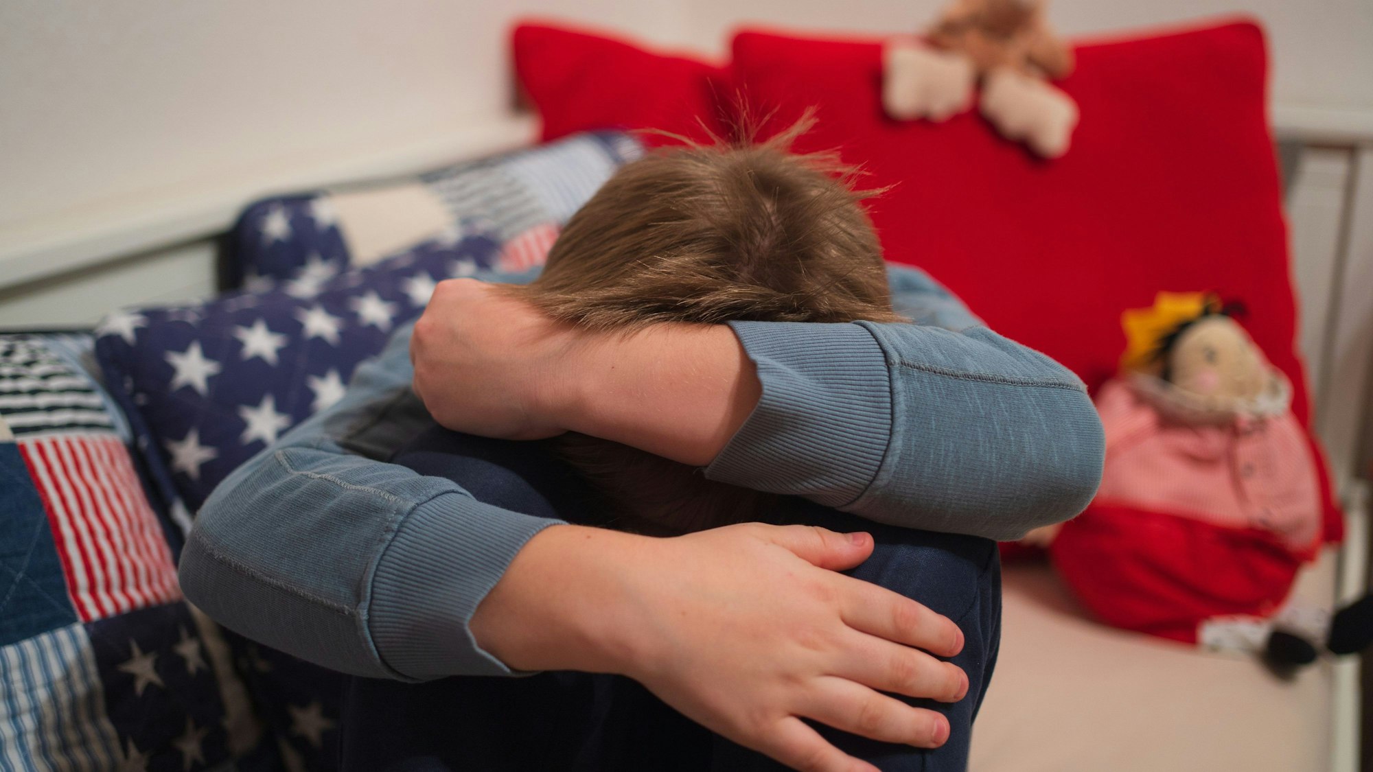 Ein Junge kauert sich auf seinem Bett zusammen.