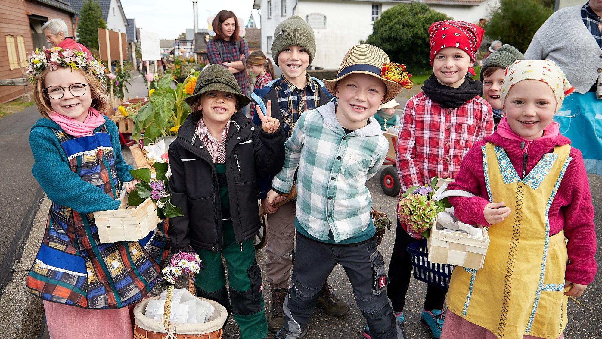 Die Kinder sind bunt kostümiert, tragen Hüte, Blumenkränze oder Kopftücher und tragen Körbe und Blumen.