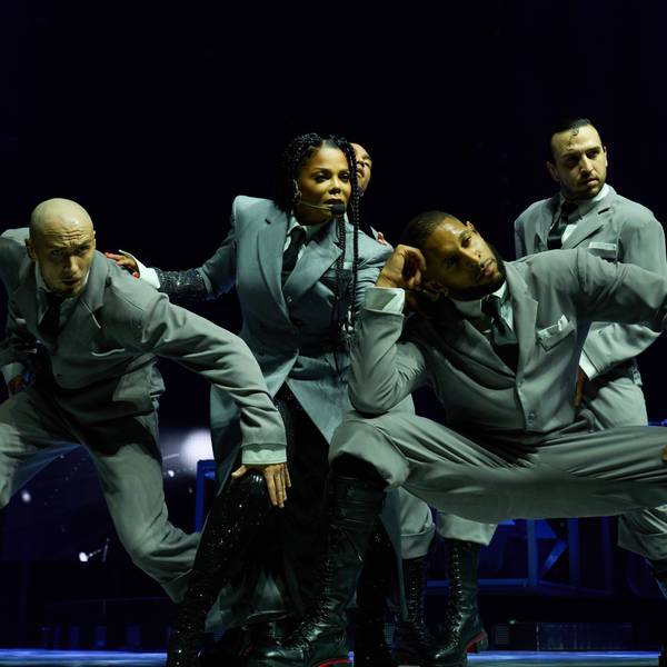 Janet Jackson posiert im stilisierten Business-Outfit inmitten ihrer Tänzer.