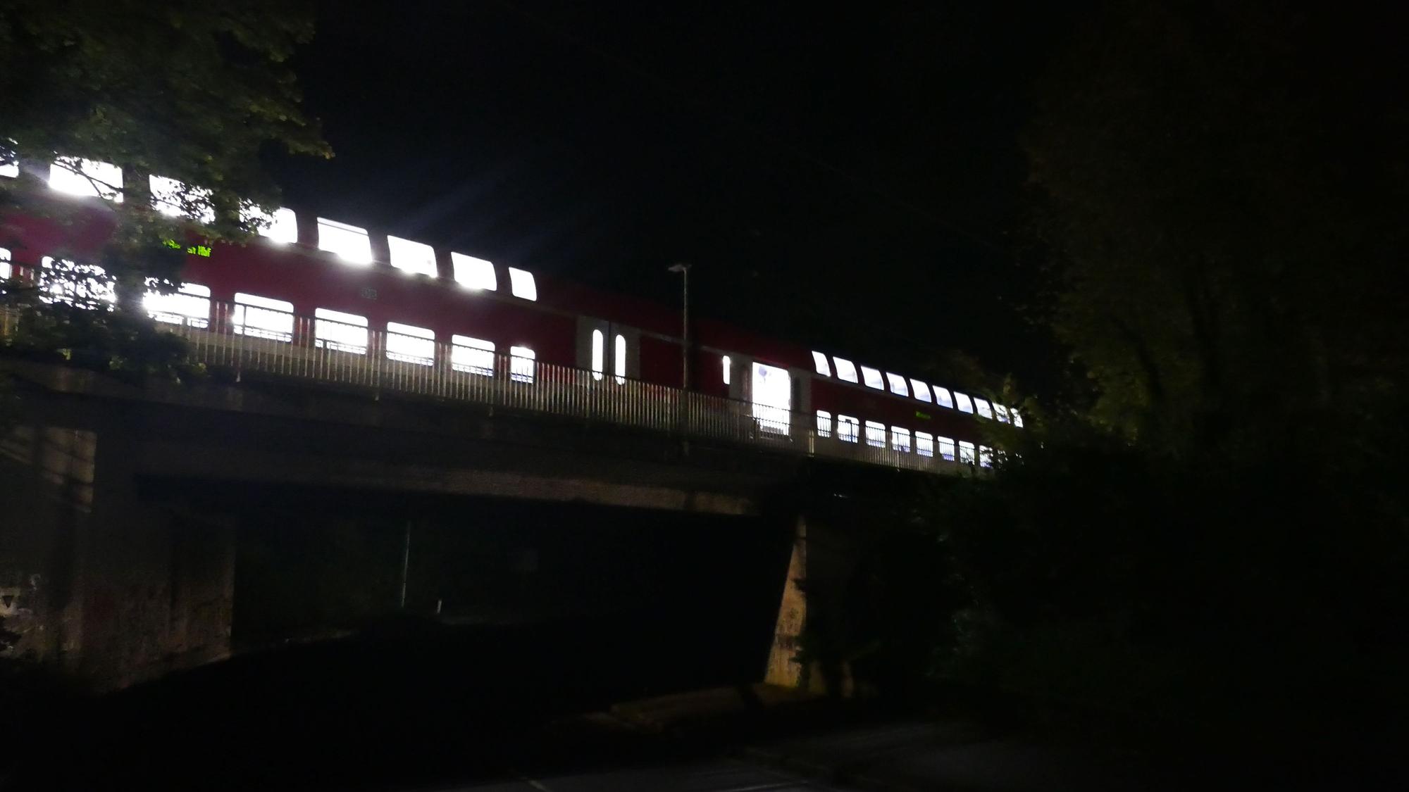 Ein beleuchteter Zug steht in der Dunkelheit auf einer Brücke.