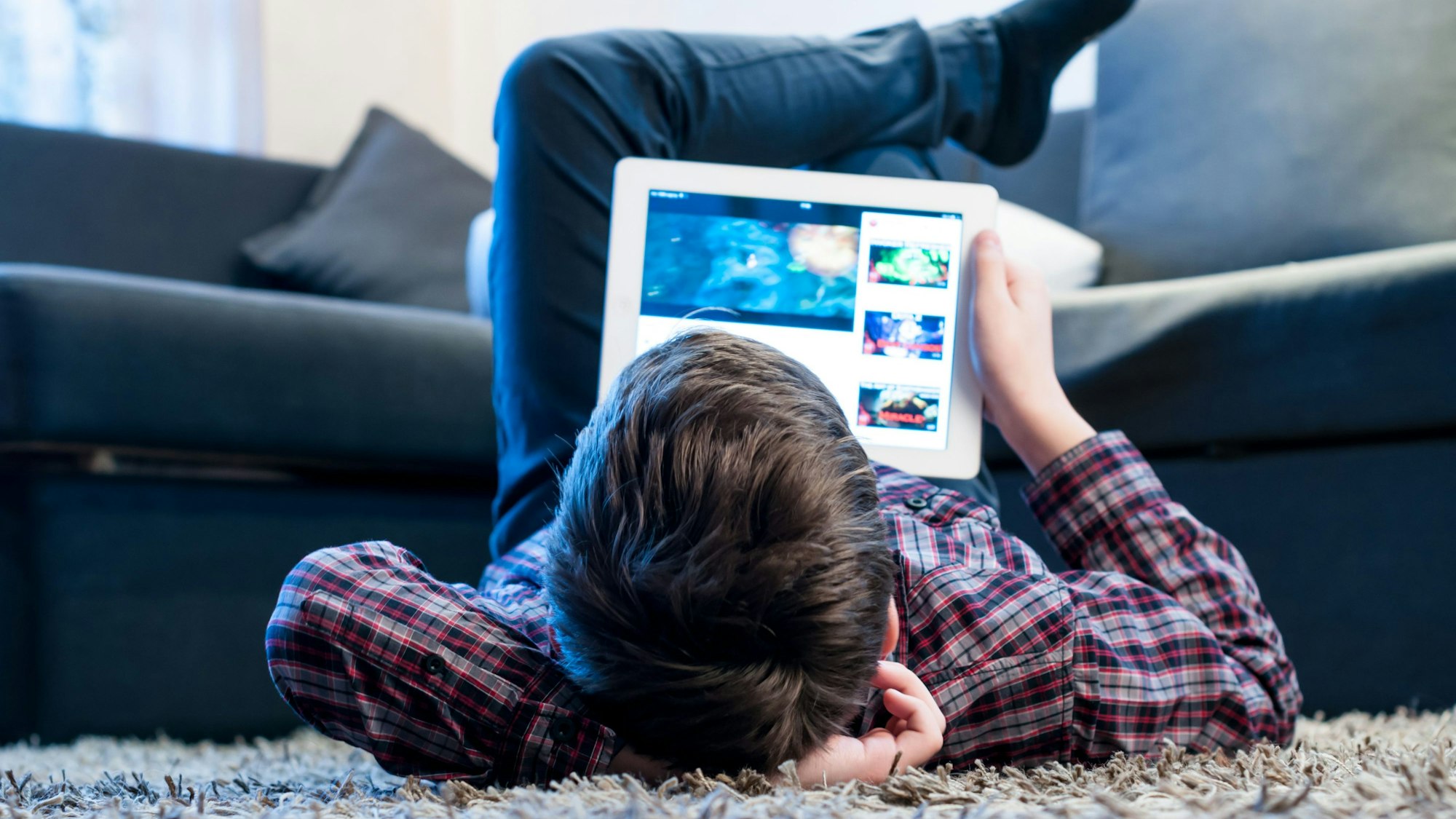 Ein Junge liegt auf dem Boden und schaut etwas in einem Tablet.