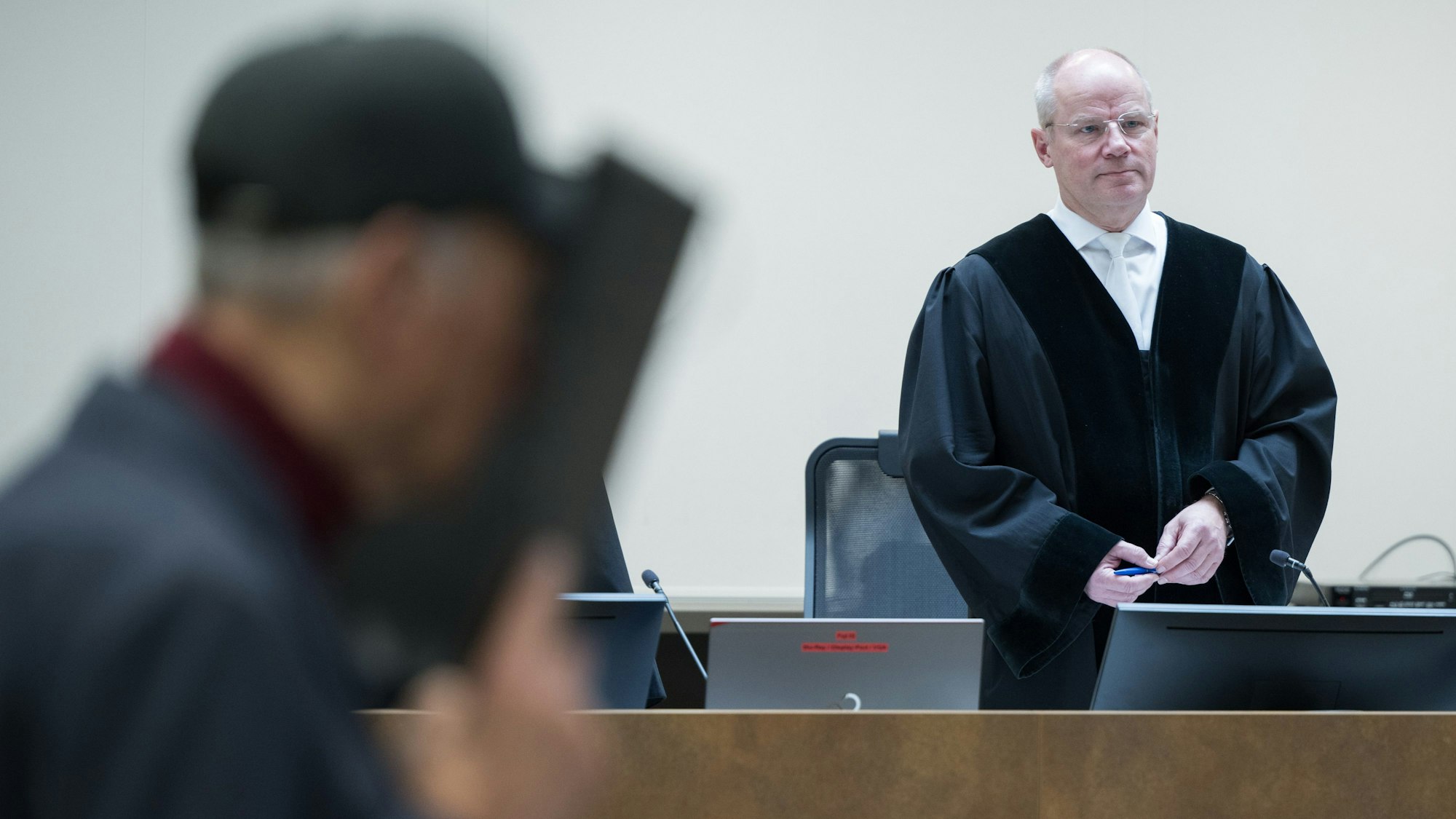 14.03.2024, Berlin: Der Angeklagte hält sich zum Beginn des Prozesses gegen den Ex-Stasi-Mitarbeiter wegen Mordes vor 50 Jahren am Kriminalgericht Moabit vor dem Vorsitzenden Richter Bernd Miczajka eine Mappe vor sein Gesicht.