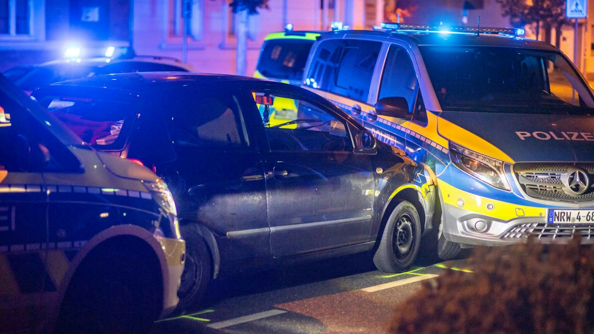 Das Bild zeigt zwei Streifenwagen, die einen schwarzen Kleinwagen an der Weiterfahrt hindern.