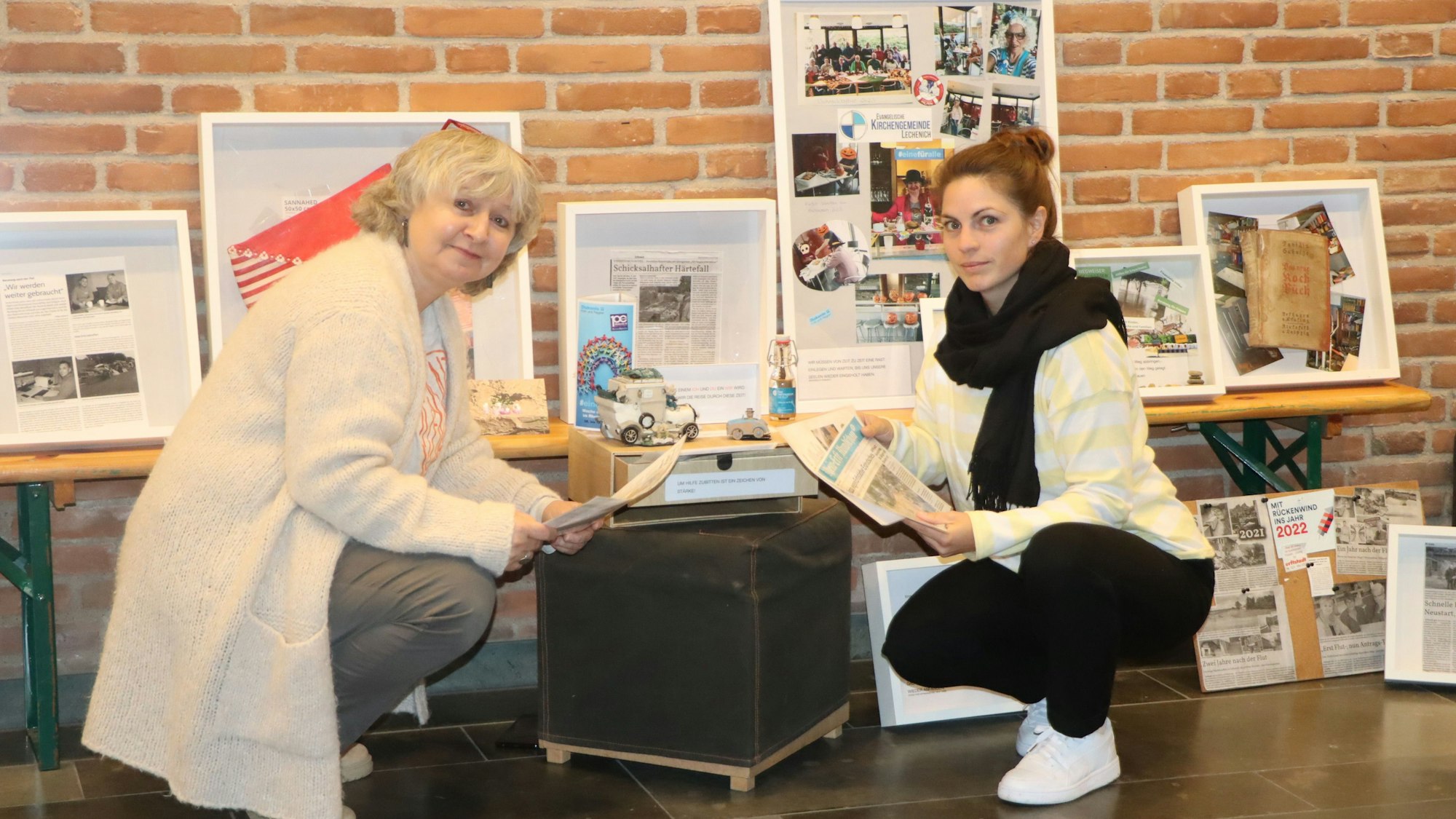 Zwei Frauen knien vor Bilderrahmen.