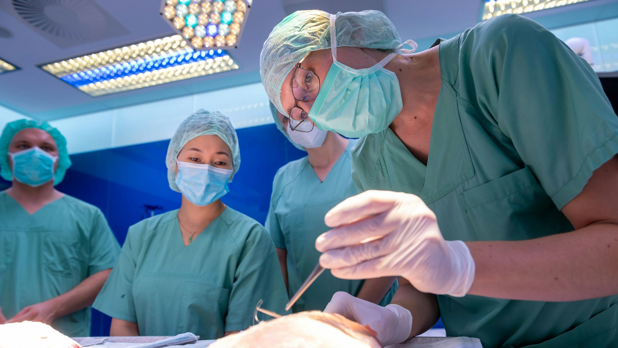 Medizinstudenten üben mit Op-Kleidung Schnitte an einer Putenbrust.