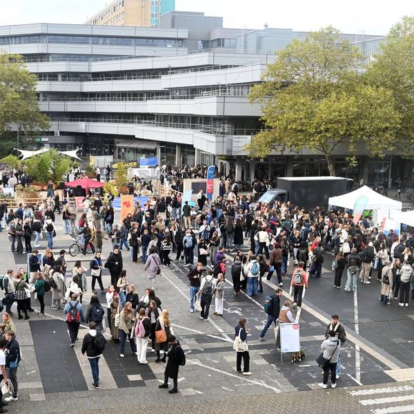 Eine Gruppe junger Leute steht auf dem Platz vor der Uni zusammen und an Ständen.