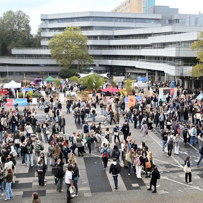 Eine Gruppe junger Leute steht auf dem Platz vor der Uni zusammen und an Ständen.