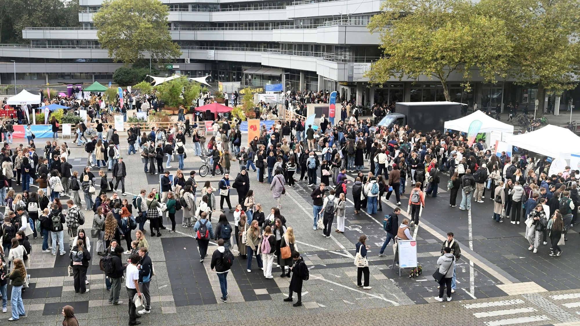 Eine Gruppe junger Leute steht auf dem Platz vor der Uni zusammen und an Ständen.