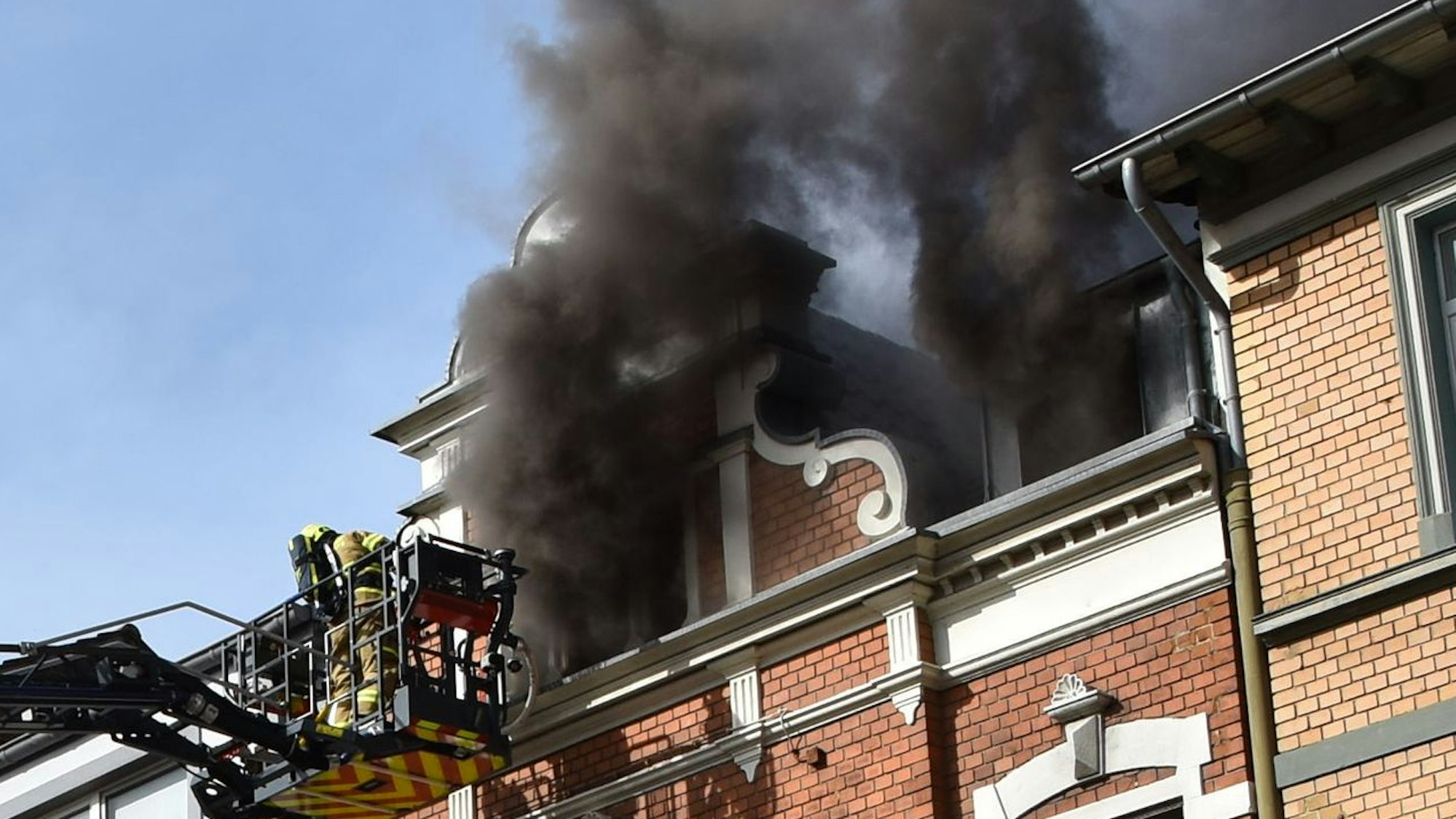 Das Bild zeigt Feuerwehrleute im Drehleiterkorb vor einer brennenden Wohnung.