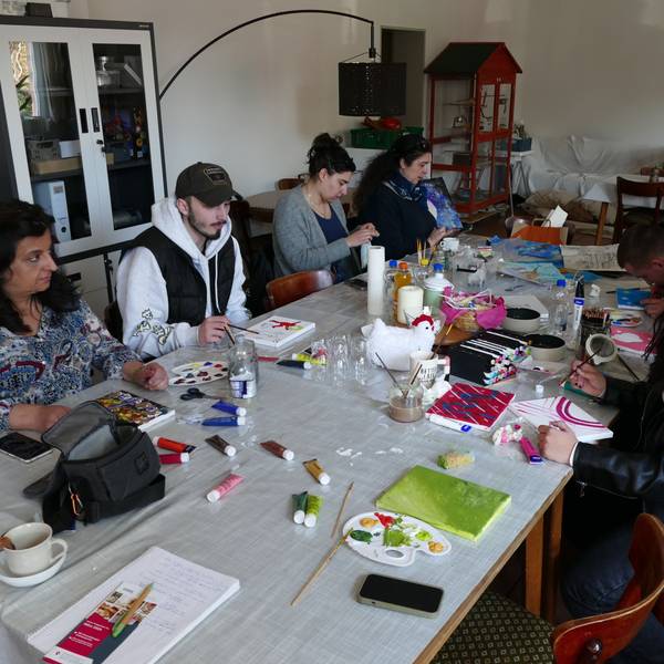 Menschen sitzen an einem klangen Tisch und malen.