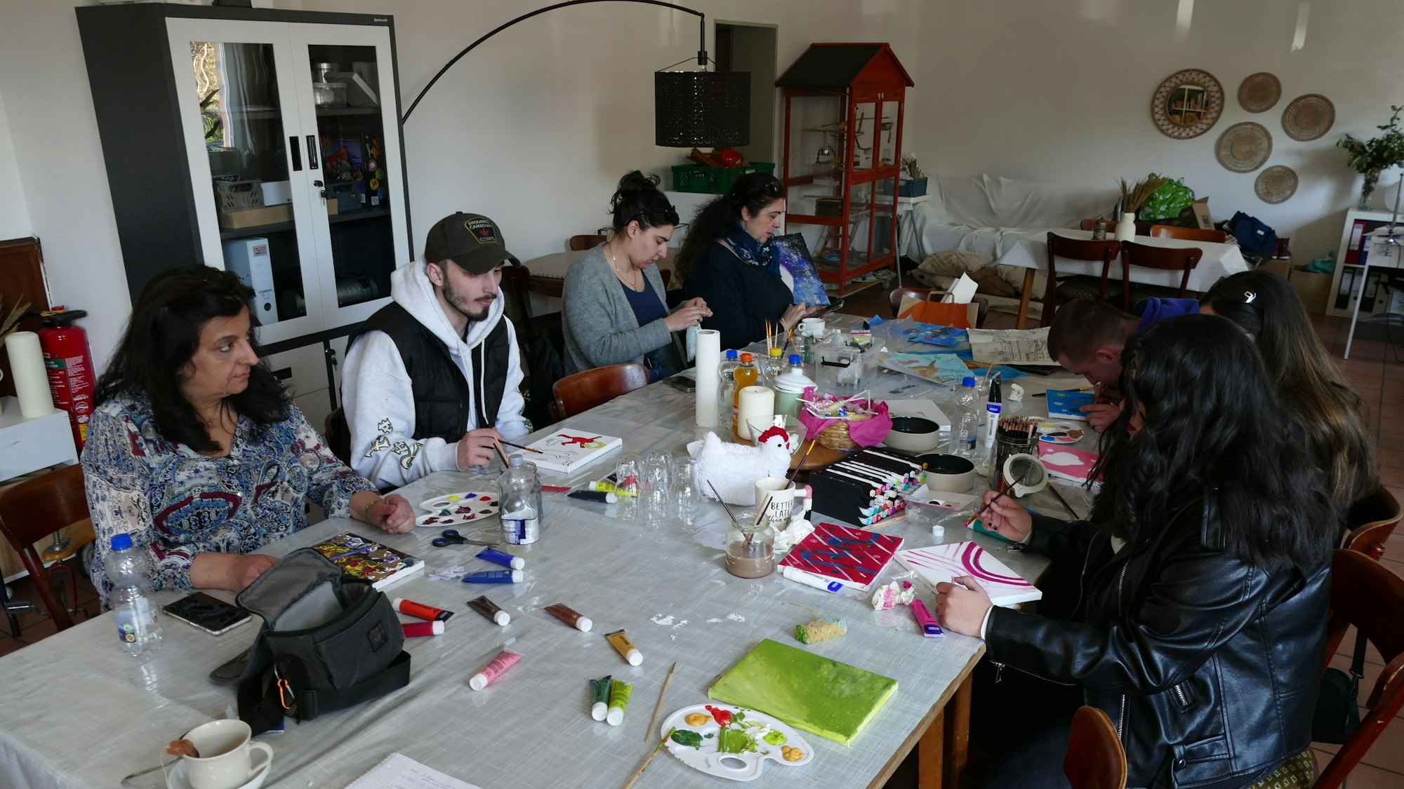 Menschen sitzen an einem klangen Tisch und malen.