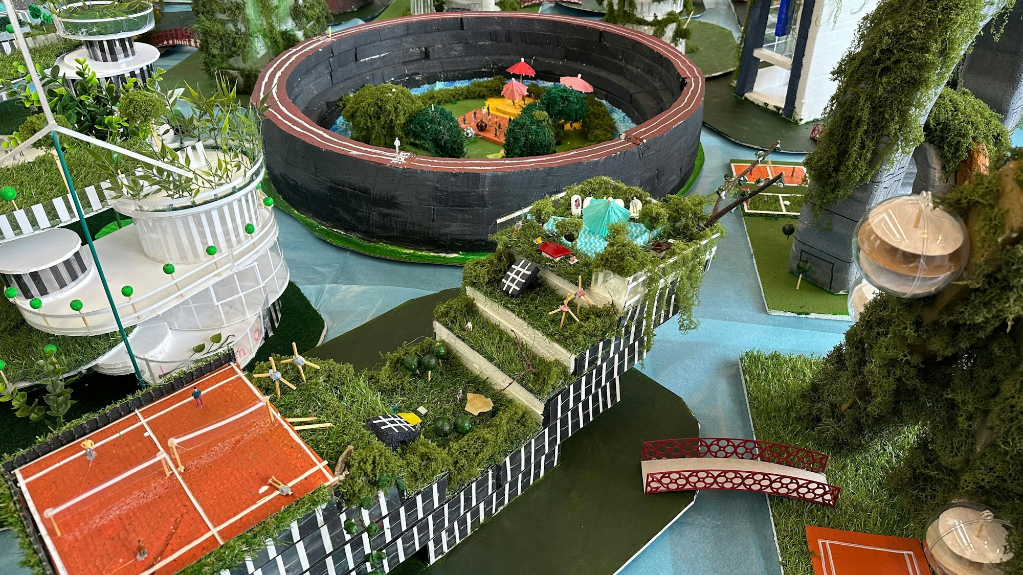 Eine Brücke führt über den blauen Schwammboden, oben im Bild die Sportarena.