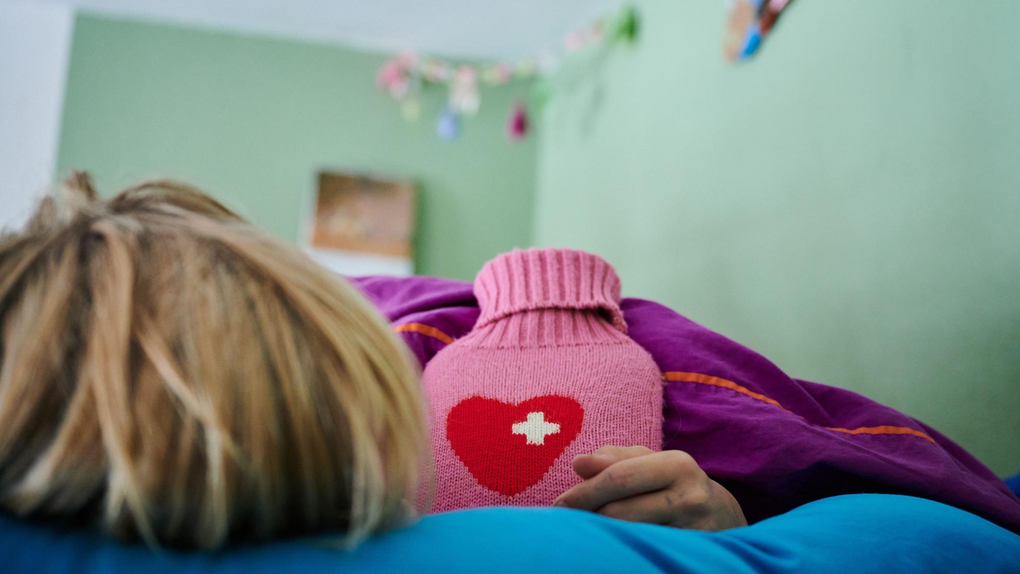 Ein Kind liegt mit Wärmflasche im Bett.
Wer eine Erkältung hat, braucht Ruhe.