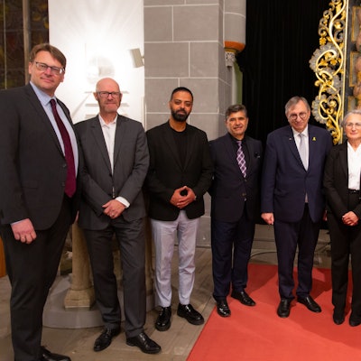 Zahlreiche Männer und einer Frau unterschiedlicher Religionen stehen bei einer Gedenkstunde in einer Kirche beisammen.