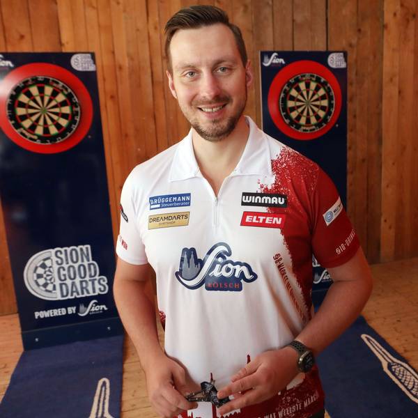 Zu sehen ist der Dartspieler Florian Hempel in der Vorderansicht. Links und rechts hinter ihm sind Dartscheiben zu sehen.