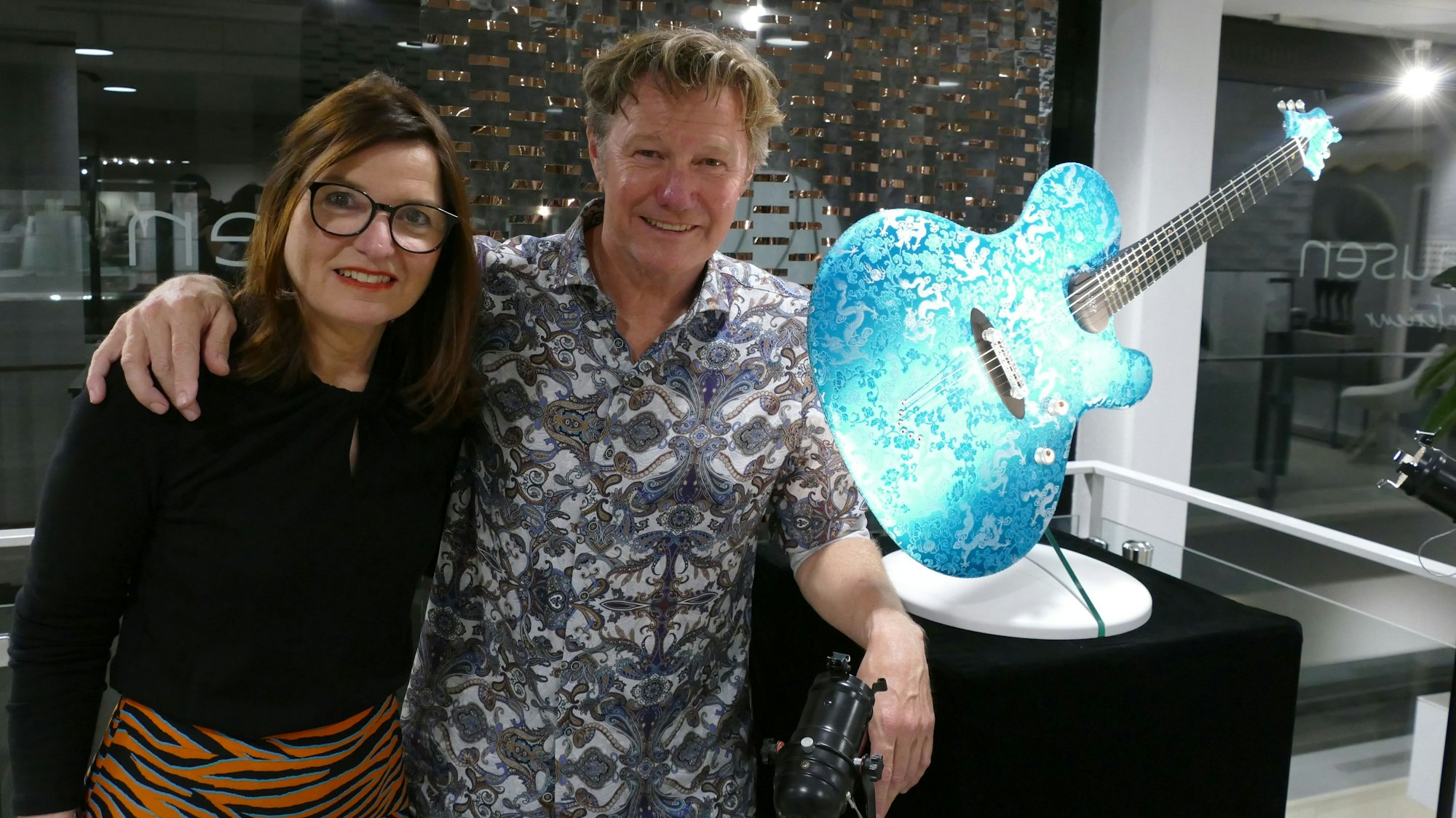Eine Frau und ein Mann stehen neben einer blauen Gitarre mit Muster.