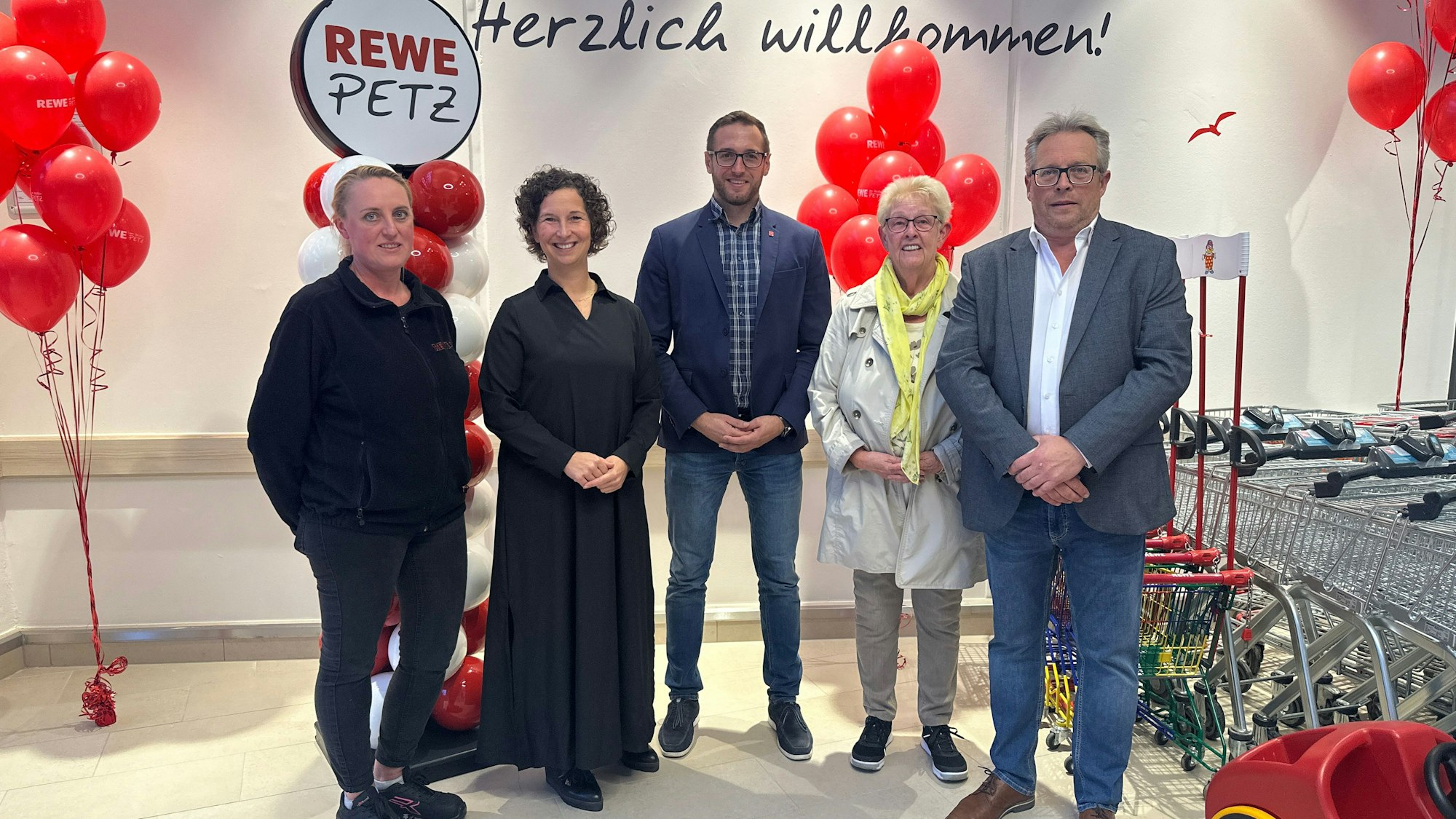 Fünf Menschen stehen zu einem Gruppenfoto aufgestellt vor weißen und roten Luftballons.