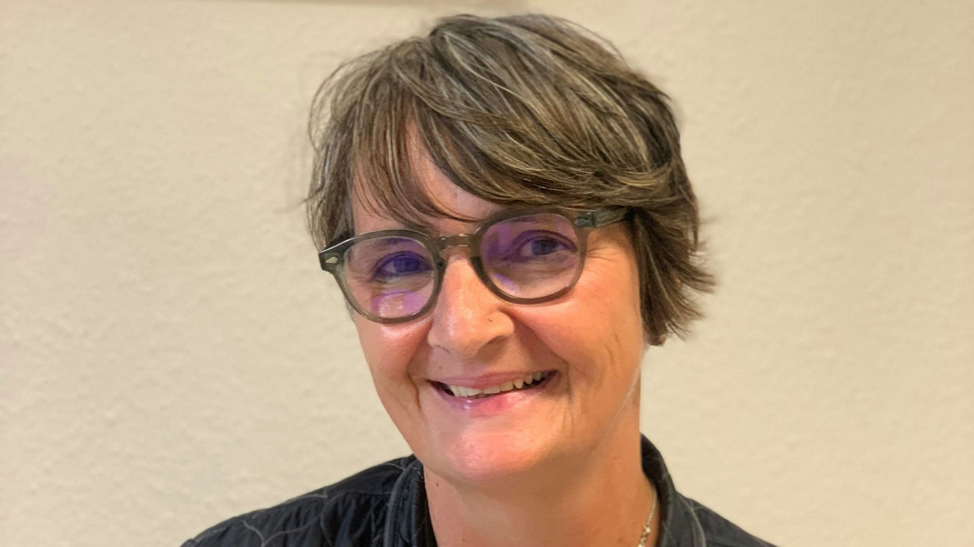 Eine Frau sitzt vor einer beigen Wand.