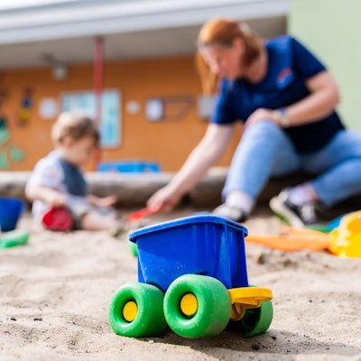 Erzieherin spielt mit einem Kind in einem Sandkasten.