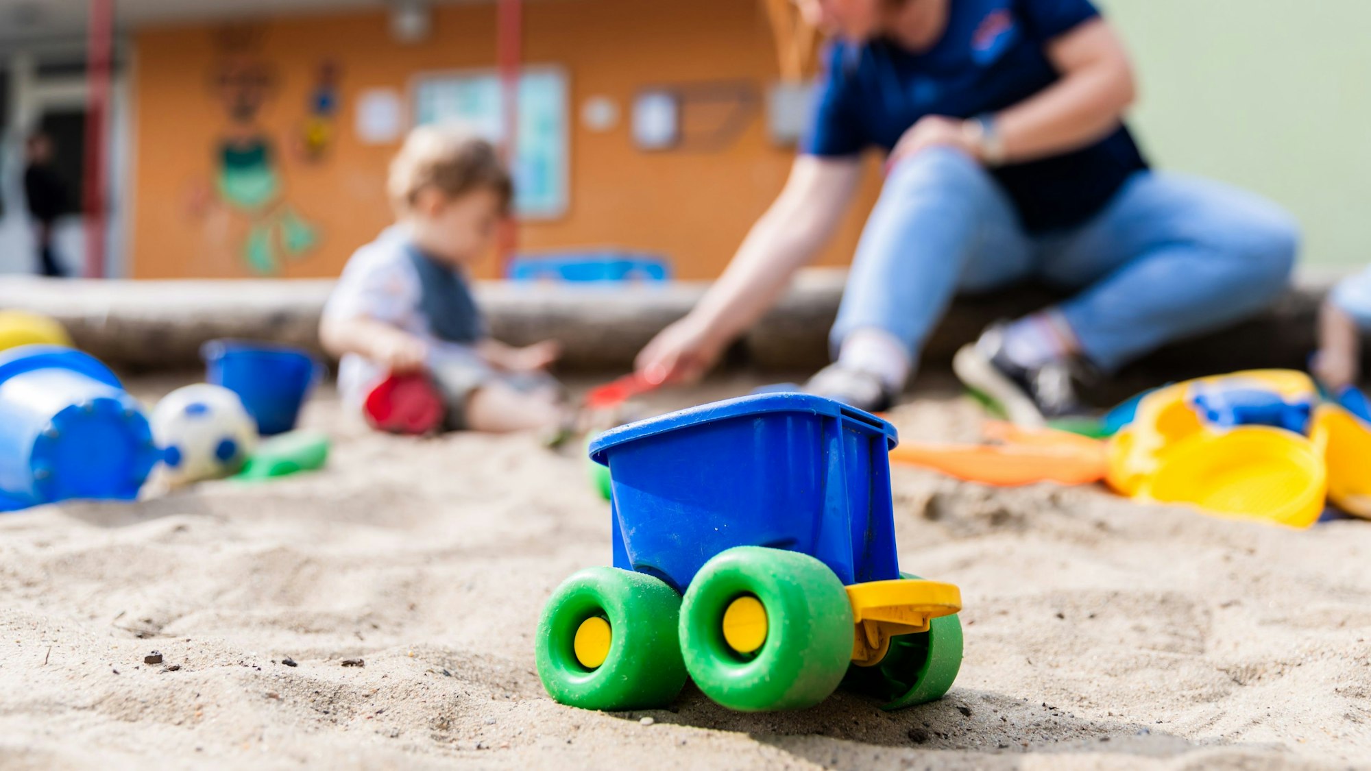 Ein Kind spielt mit einer Erzieherin im Sandkasten einer Kita.