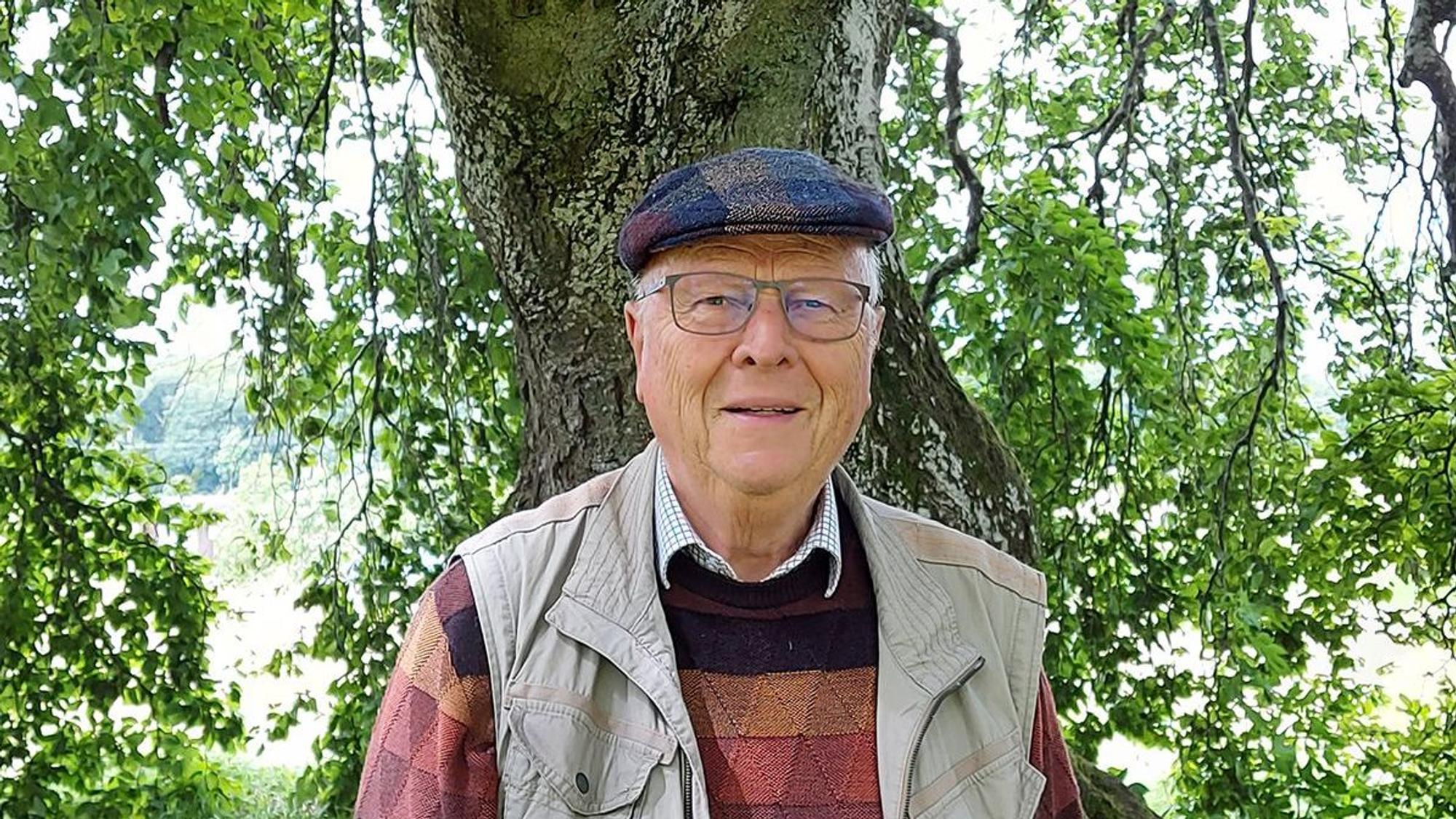 Das Bild zeigt Wolfgang Schumacher vor einem Baumstamm.