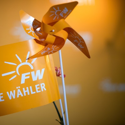 Ein orangefarbenes Fähnchen mit dem Aufdruck „Freie Wähler“ steht neben einem orangefarbenen Windrädchen.