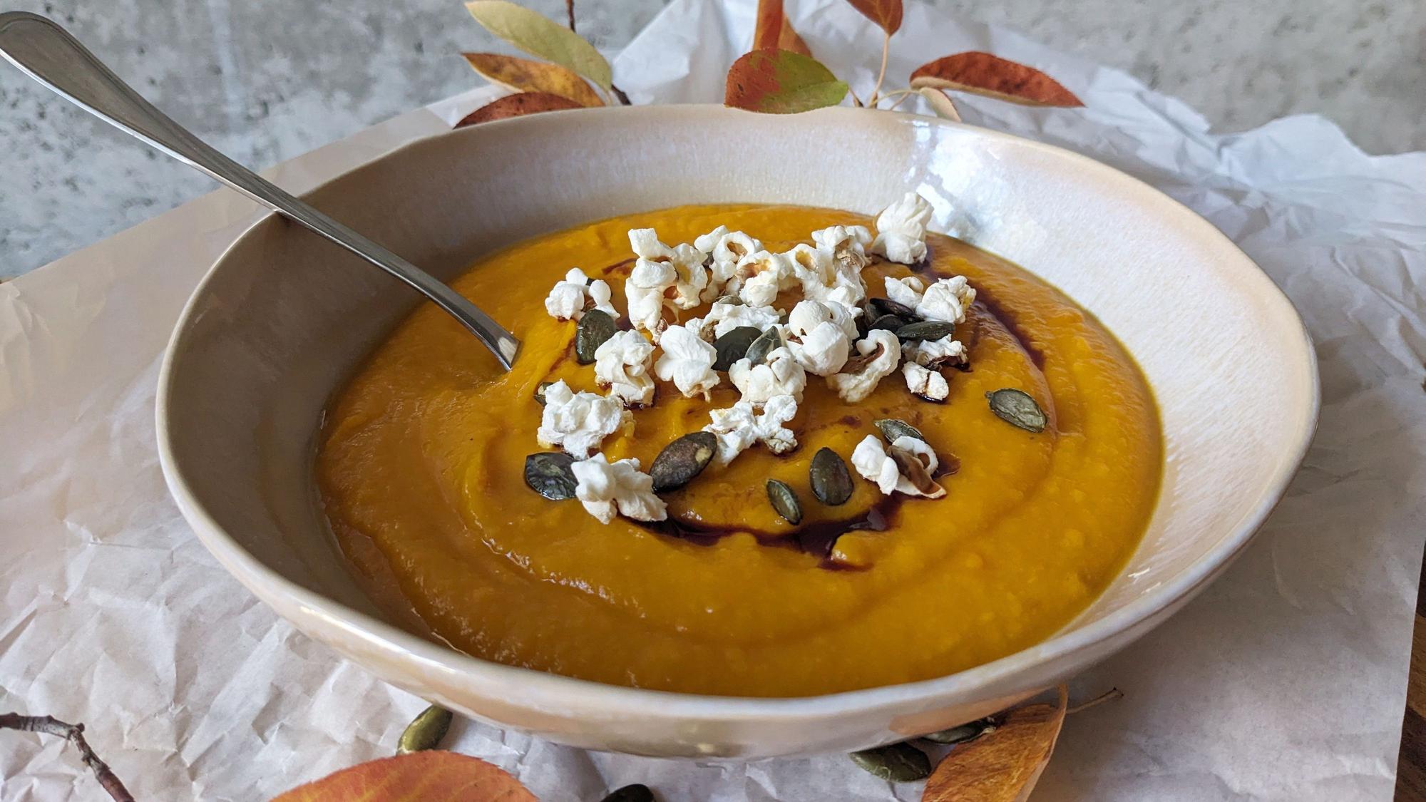 Eine Schüssel mit Kürbissuppe, die mit Popcorn, Kürbiskerne und Kürbiskernöl verziert ist.
